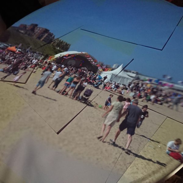 An image taken at the First Light Festival. The image is a projection from the nomadic camera obscura owned by Gainsborough's house. There are lots of people on a sandy beach and various tents around.