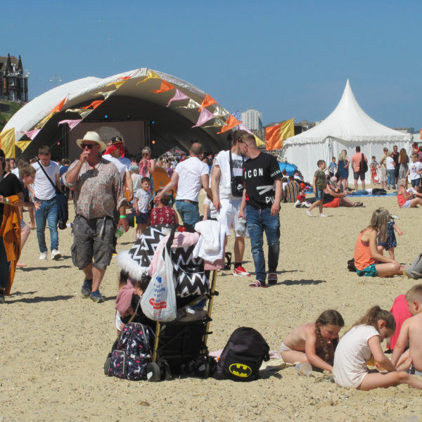 An image taken at the First Light Festival. There are lots of people on a sandy beach and various tents around.
