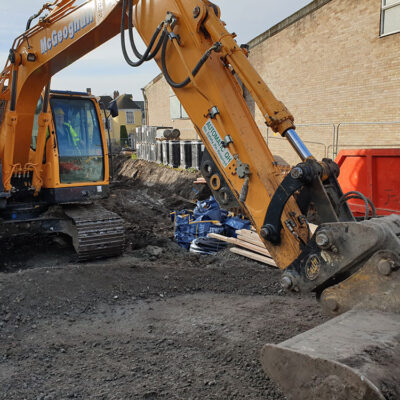 An image of a yellow digger is in main focus. It is digging in the dirt in front of it.