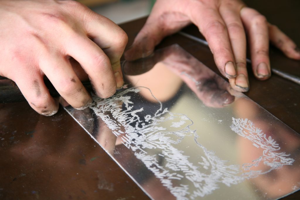 An image of someone etching a plate with an etcher's burin.