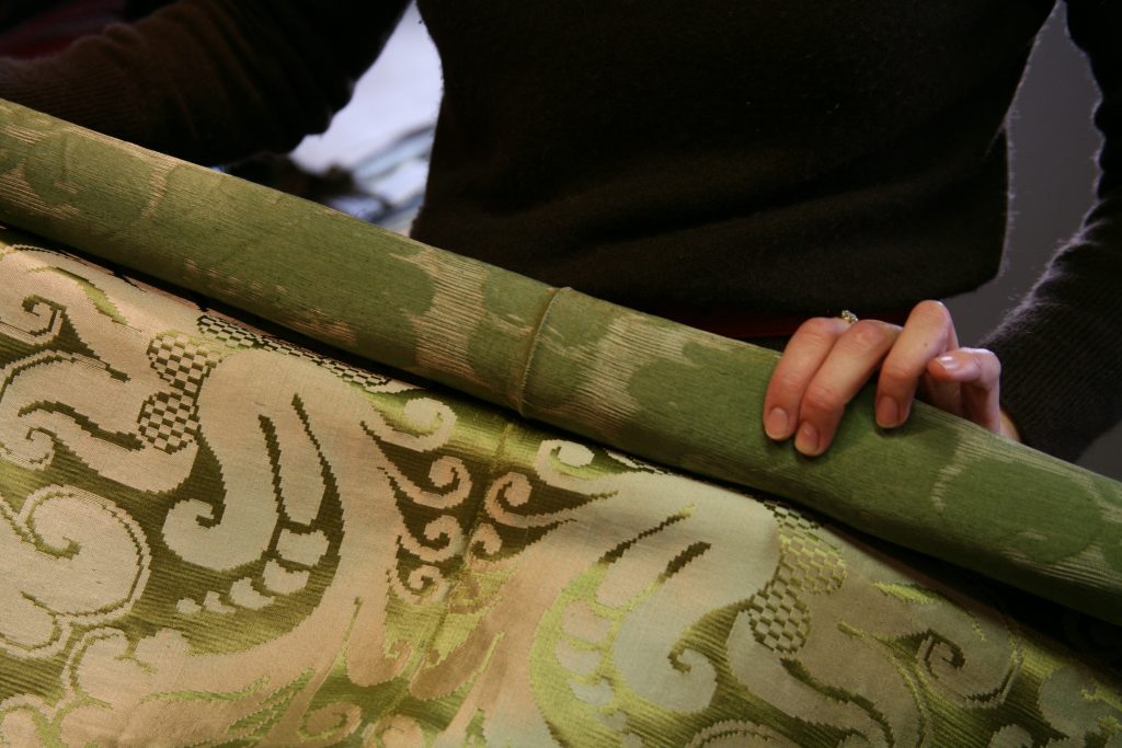 An image of someone holding up a roll of green silk damask.