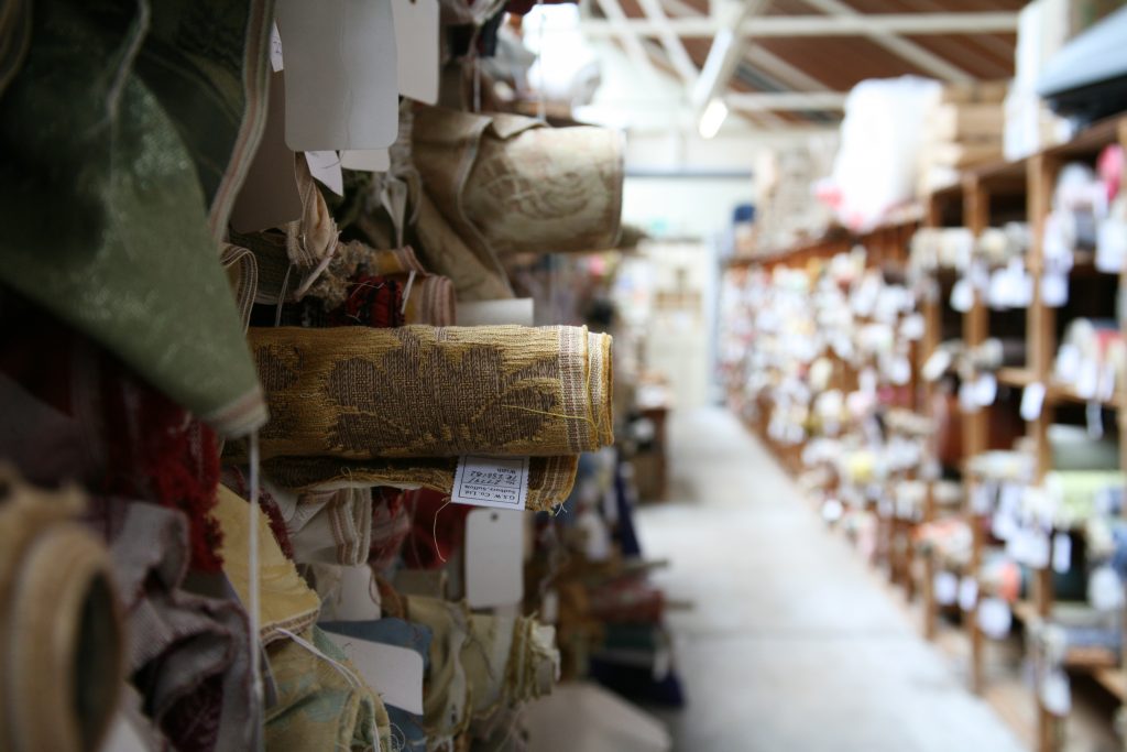 An image taken at a silk mill in Sudbury. The image is focused on a shelf stacked with rolls of silk damask.