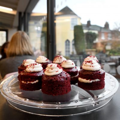 An image taken within The Watering Place café at Gainsborough's House. It shows red velvet cupcakes on a dish in front of visitors enjoying their coffee and lunch.