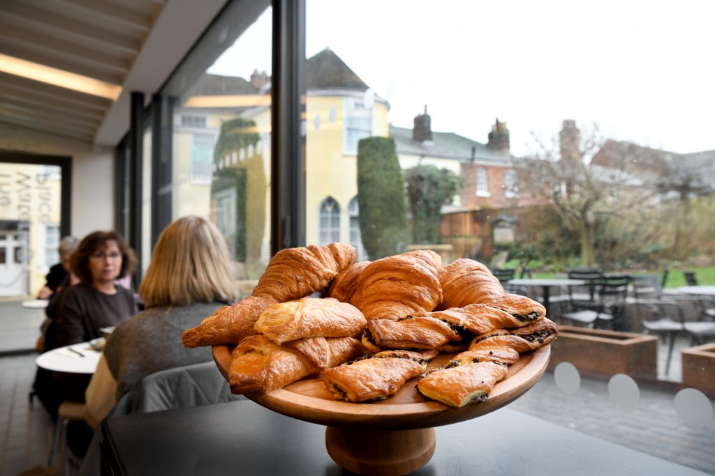 An image taken within The Watering Place café at Gainsborough's House. It shows a batch of freshly baked pastries on display in front of the old House.