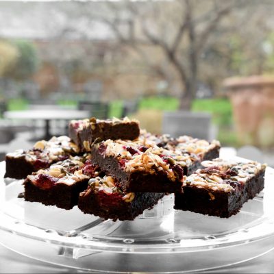 An image taken within The Watering Place café at Gainsborough's House. There are freshly baked, gluten-free brownies on a serving plate in front of the gardens.