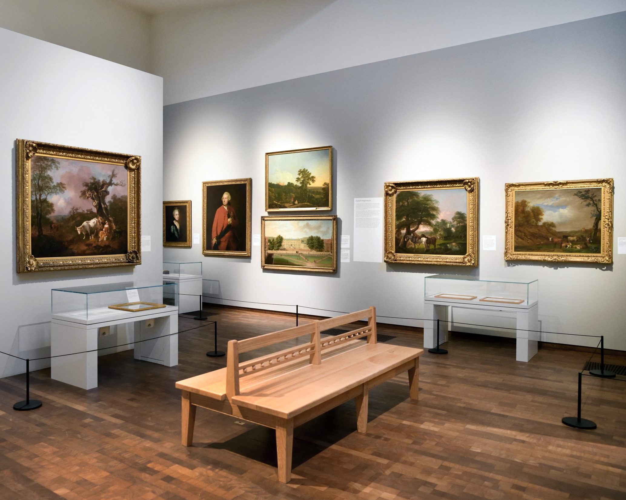 An image taken within the Timothy & Mary Clode Gallery of the Woburn exhibition.It shows a series of masterpieces on the wall and artefact cabinets, as well as a Suffolk style bench in the centre.