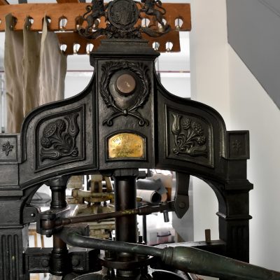 An image of a victorian printing press in the Print Workshop at Gainsborough's House. It is black with intricate embossed detais and gold plated plaques.