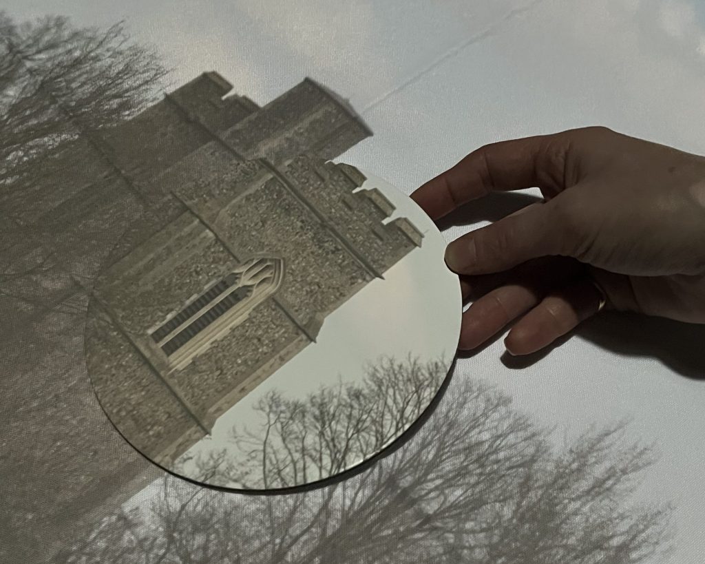 An image of a church being projected through the Camera Obscura. A hand is holding a circular canvas bringing the details of the church and trees around it into focus.