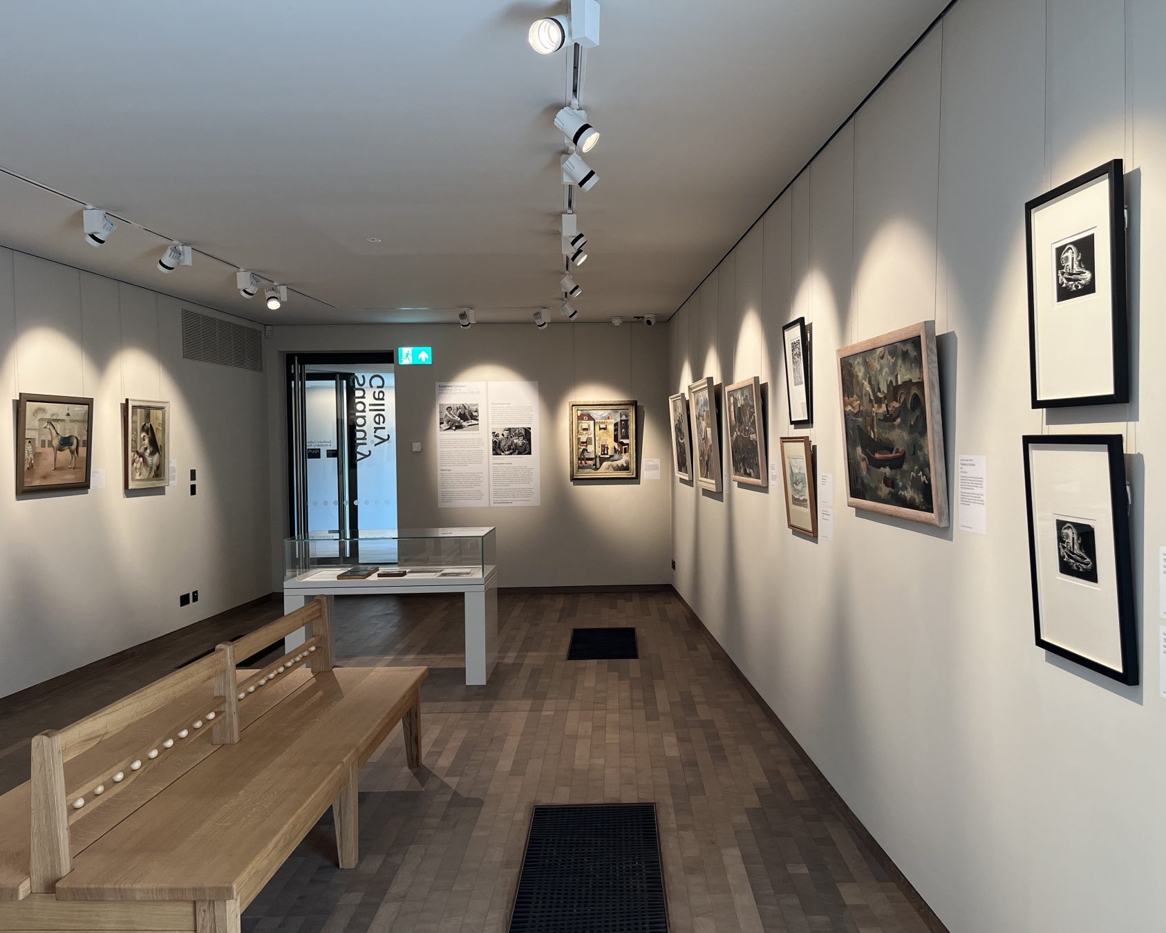 An image taken in the Sudbury Gallery at Gainsborough's House. The exhibition is 'Suzanne Cooper: Paintings and Wood Engravings, 1935–39'. There are various pieces of artwork on display on walls and in cabinets.