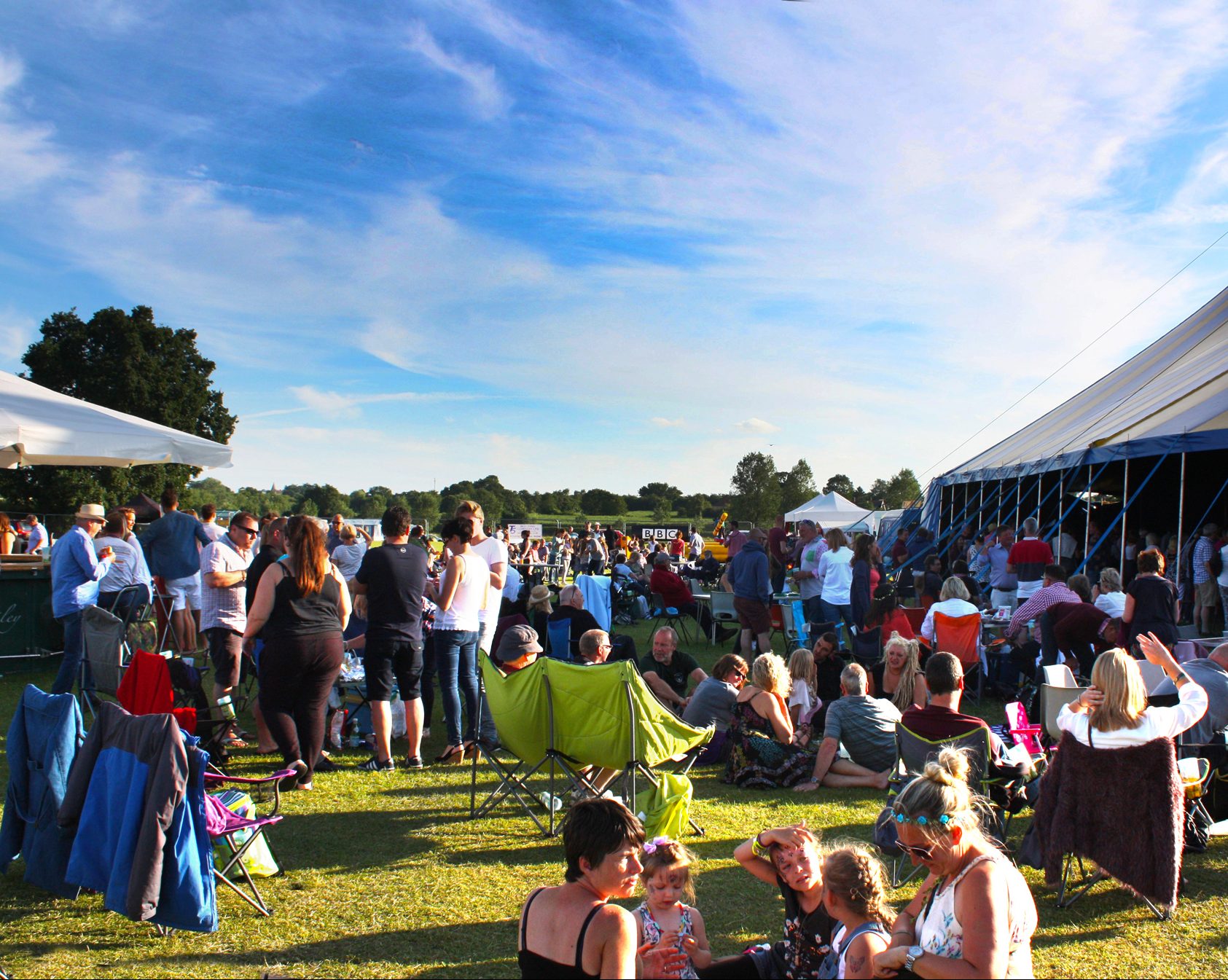 An image of lots of people crowding at Bures Music Festival. There is a blue sky in the background.