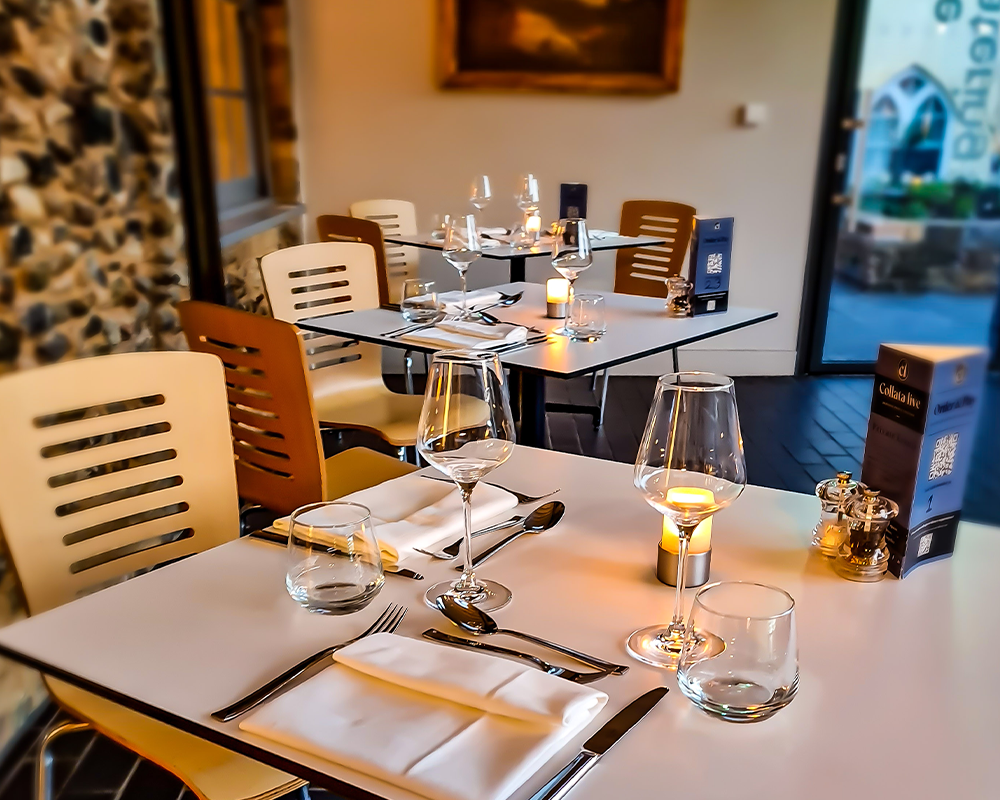An image of various tables set for an evening dining experience in The Watering Place café, Sudbury. There are wine glasses, candles and serviettes displayed on the tables.