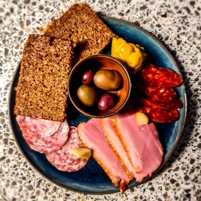 An image of one of the courses from the evening dining experience at The Watering Place café in Sudbury. There are various cold meat cuts, olives, picallily and rye bread on a large dinner plate.