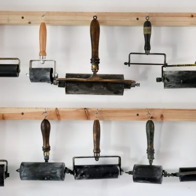 An image of various sized ink rollers hung on a wall.