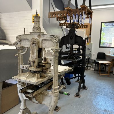 An image of two of the printing presses in the Print Workshop at Gainsborough's House, Sudbury. They are Victorian. There are various prints hung above them.