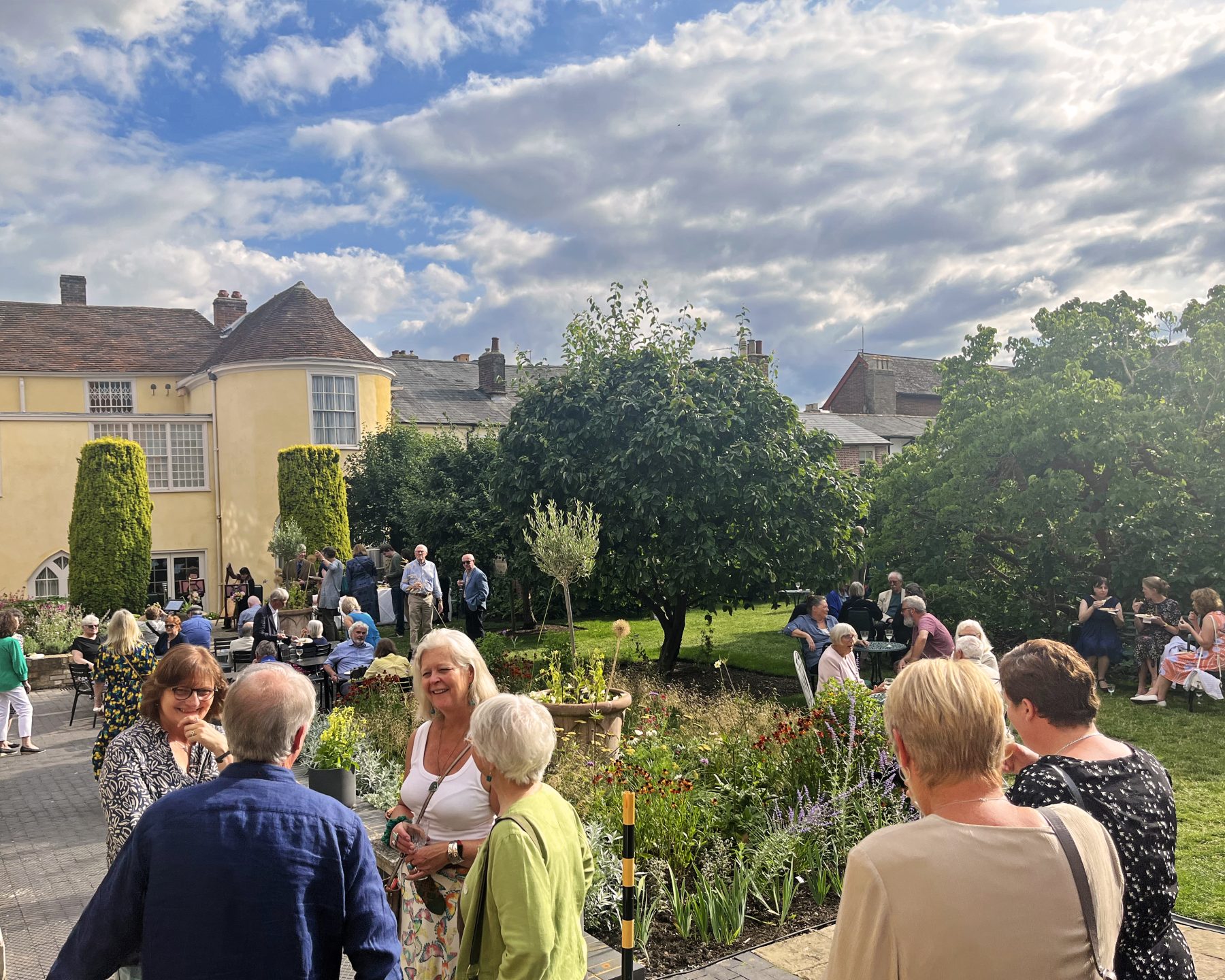 An image taken at the Annual Friends Garden Party at Gainsborough's House in 2023. There are lots of groups of people enjoying themselves in the sun.