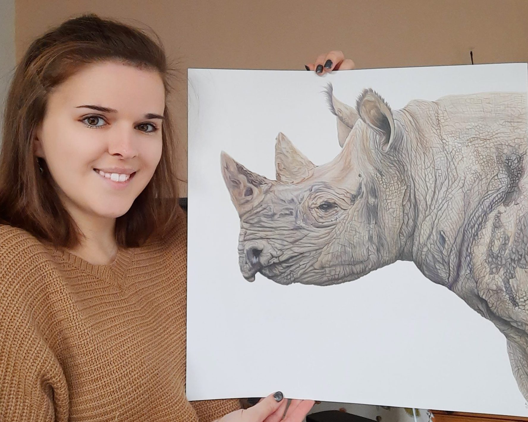 Lucy Webster is holding up a Rhino Portrait on paper.