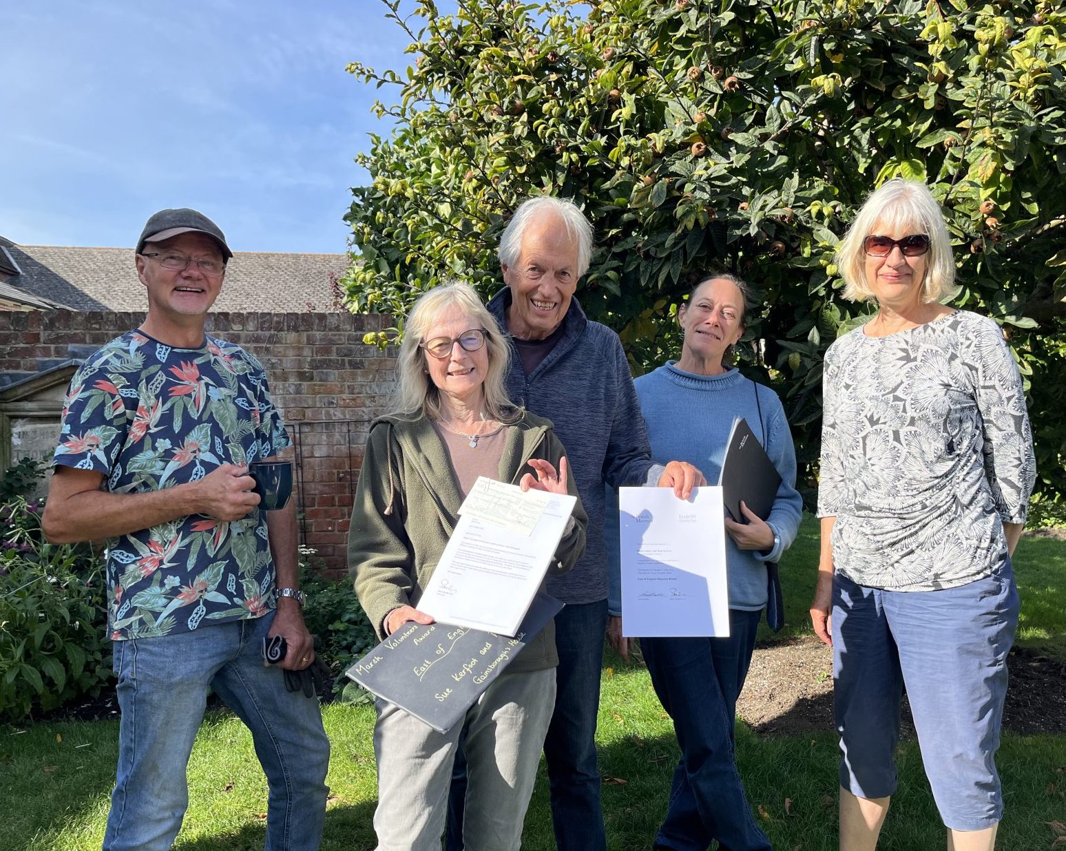 An image of some of the Gainsborough's House Garden Volunteers holding up an award certificate and smiling to camera in the garden.