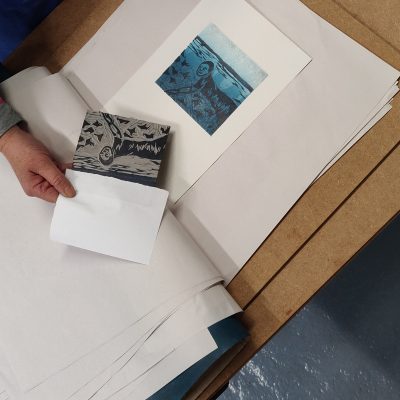 An image of a person revealing a lino cut print. The print is blue.