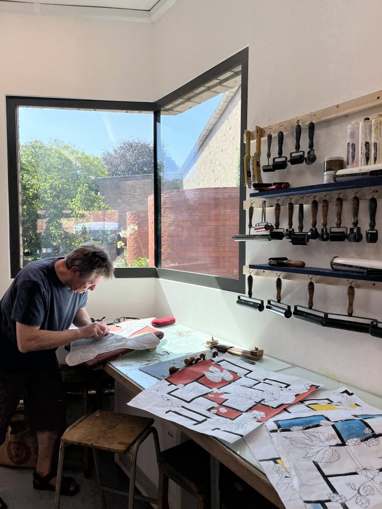 An image of a Print Workshop member using the studio to produce a lino print. There is a window shining light on them from behind.