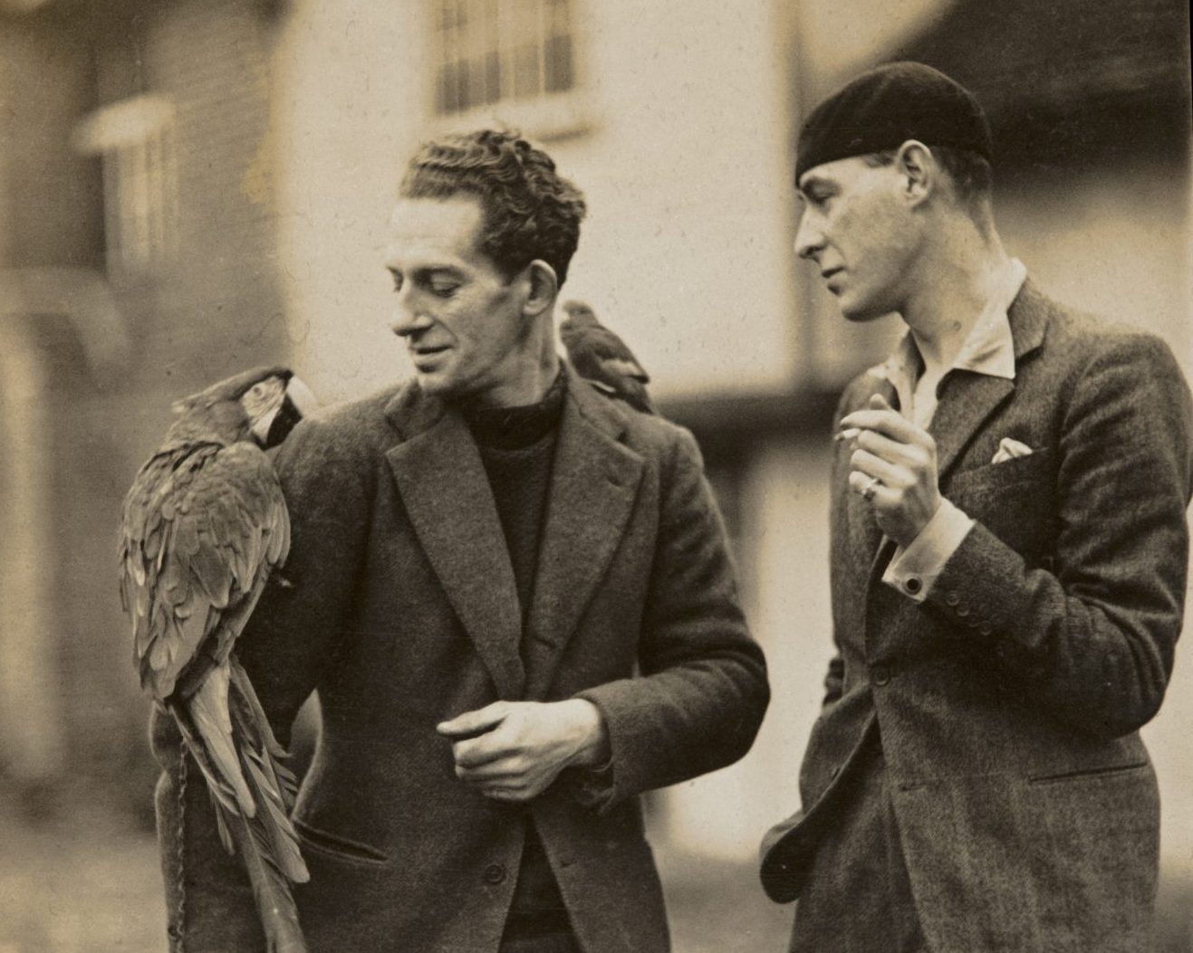 A sepia image of Cedric Morris and Arthur Lett-Haines. Cedric has a parrot on his shoulder and Lett-Haines is smoking a cigarette. They are both wearing suits.