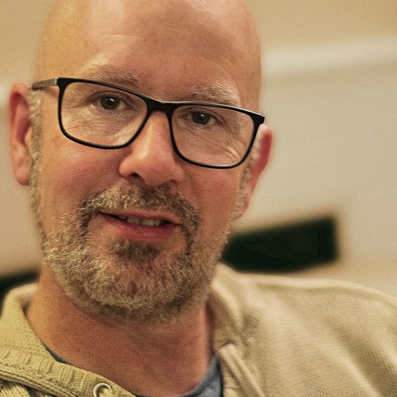 An image of Simon Edge. A white man who is bald with a beard. He is wearing glasses.