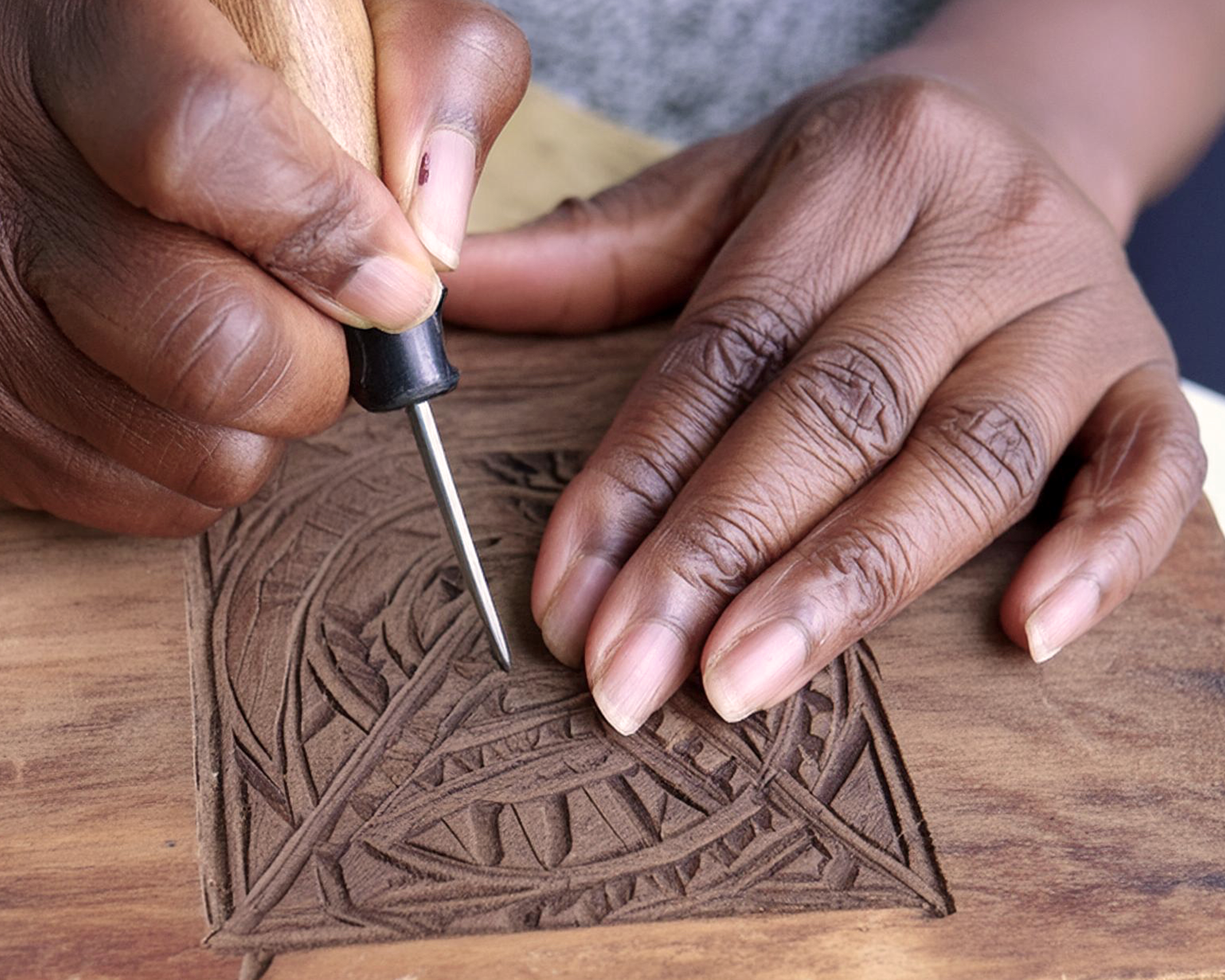 An image of a black woman using an engraving tool to cut a woodblock design for printmaking.