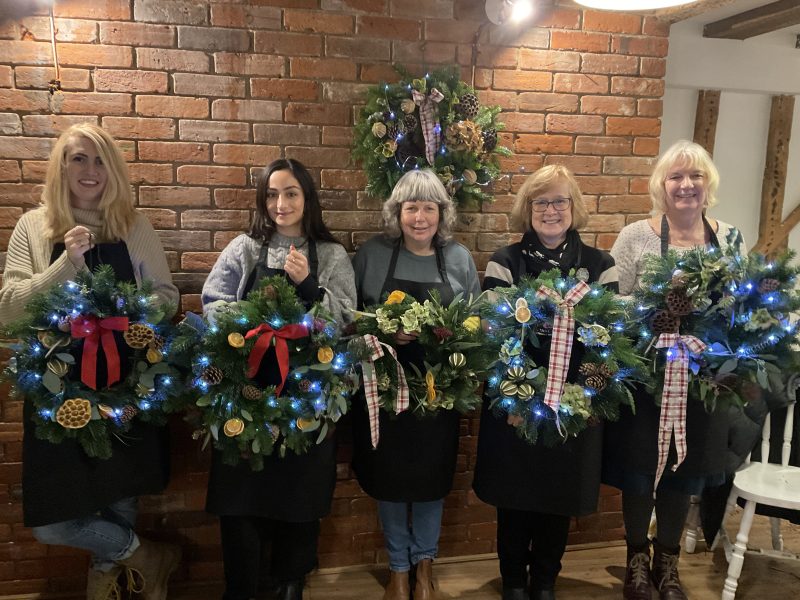 An image of 5 women holding up their handmade wreaths. 