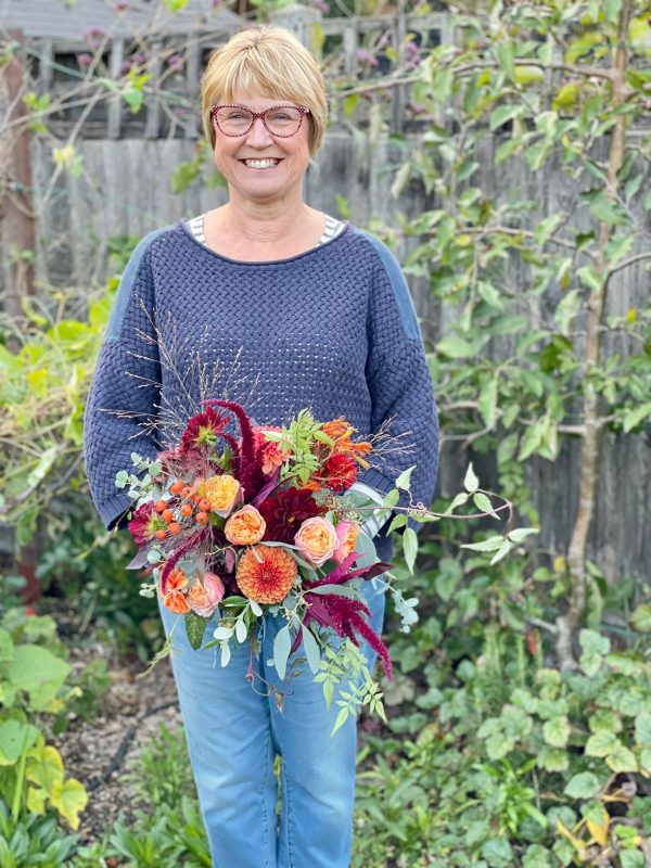 An image of Just Anne Flowers holding a handmade wreath in the garden. 